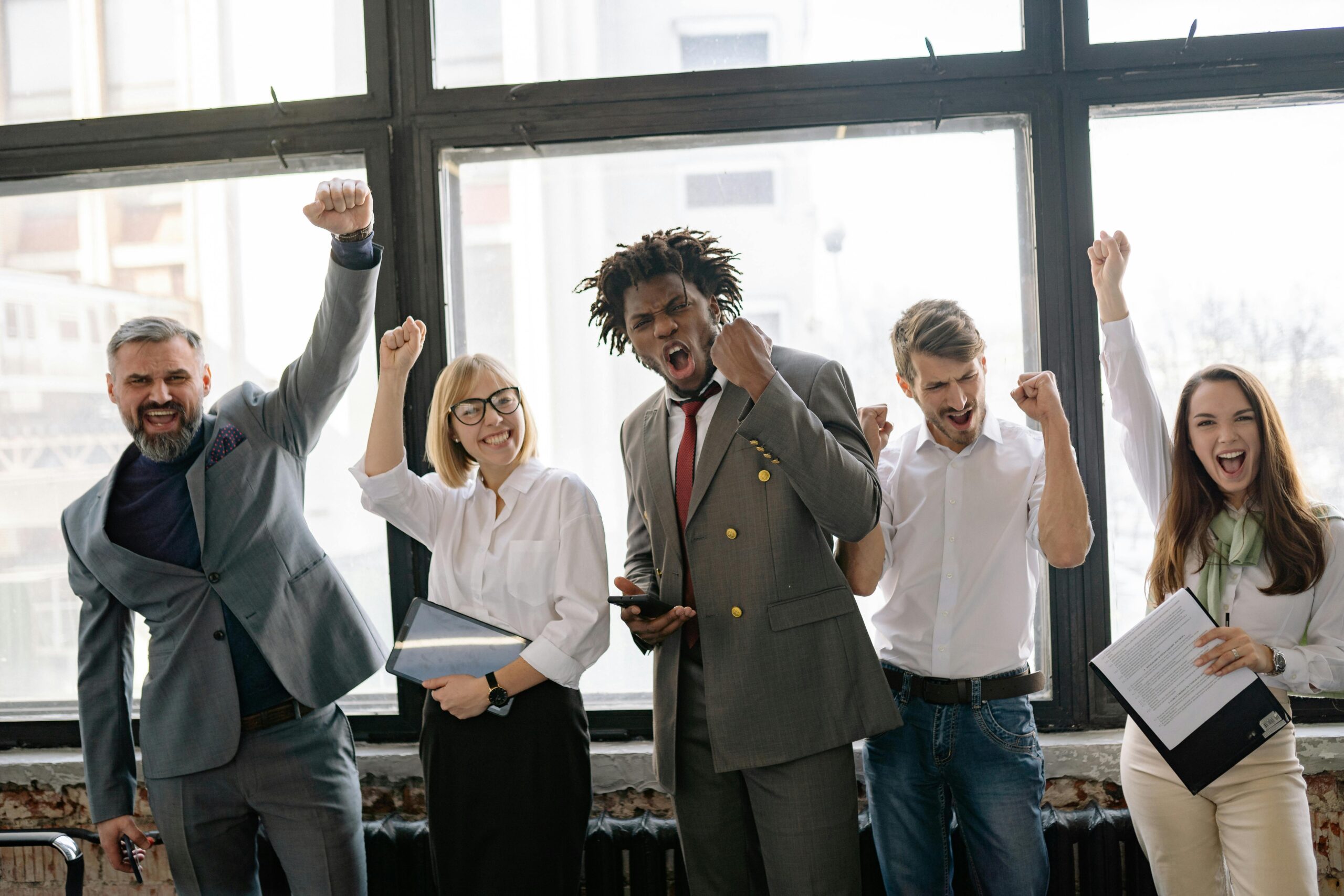 Group of diverse professionals celebrating achievement in office setting with enthusiasm.