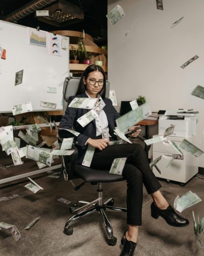 Woman Sitting on an Office Chair with Money Flying All Around Her